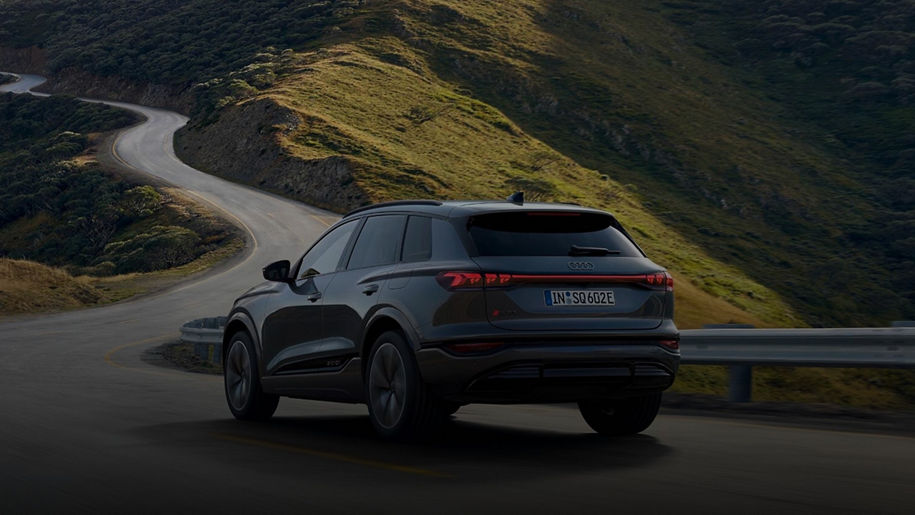 An Audi vehicle driving along a road in a hilly landscape